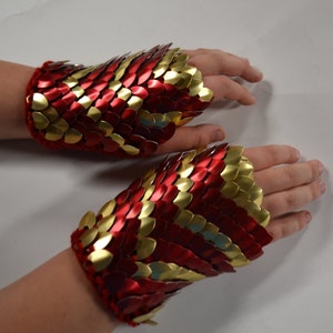 May include: A pair of red and gold fingerless gloves made of chainmail. The gloves are made of small, overlapping metal scales.