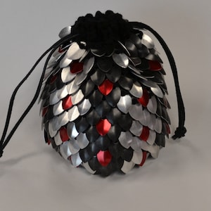 Peut inclure: Un sac à dés en forme d'écailles de dragon noir, argenté et rouge avec un cordon de serrage noir.