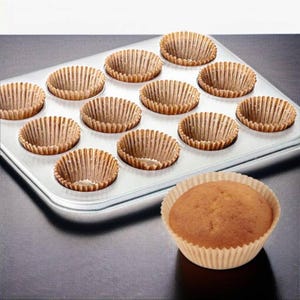 May include: A metal muffin tin with 12 empty brown paper liners. One baked muffin in a paper liner sits outside the tin. The liners are ribbed and ready for baking. Baking supplies.