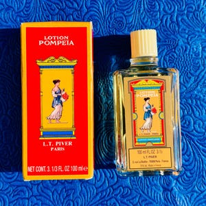 May include: A vintage bottle of "Lotion Pompeia" perfume and its box. The box is red with gold trim and features an illustration of a woman in a classical gown. The bottle is clear with a cream-colored cap and a matching label. The bottle contains 100 ml (3.3 fl oz) of perfume.