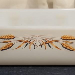 May include: Rectangular white baking dish with wheat design. The dish has a slightly curved rim and handles on each end. The wheat design features golden and brown wheat stalks in the center of the dish.