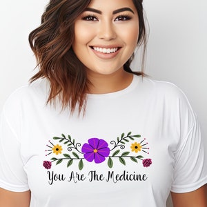 May include: White t-shirt with a floral design and the text "You Are The Medicine".