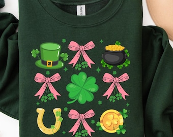 May include: A forest green sweatshirt with a festive St. Patrick's Day design. The design features a leprechaun hat, shamrocks, gold coins, a horseshoe, and pink bows.
