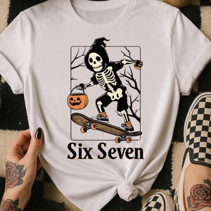 May include: White t-shirt featuring a Halloween-themed graphic. The design includes a skeleton skateboarding and holding a jack-o'-lantern. The text "Six Seven" is printed below the graphic. The shirt is styled with black and white checkered shoes.