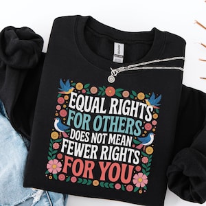 May include: Black sweatshirt featuring the text "EQUAL RIGHTS FOR OTHERS DOES NOT MEAN FEWER RIGHTS FOR YOU" in white and red, with floral and bird illustrations. A silver necklace is draped across the sweatshirt.