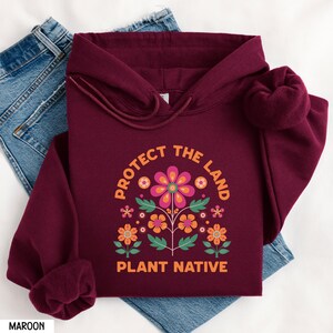 May include: Maroon hoodie with a floral design and the text "Protect the Land Plant Native".