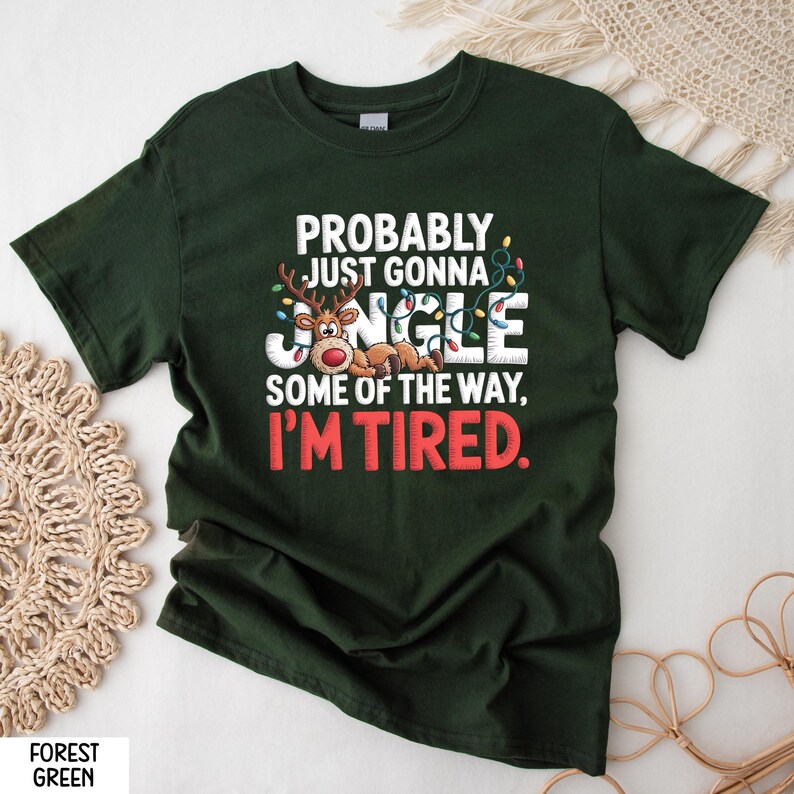 May include: Forest green t-shirt featuring the text "PROBABLY JUST GONNA JINGLE SOME OF THE WAY, I'M TIRED." The design includes a reindeer, Christmas lights, and the word "JINGLE" in a festive font.