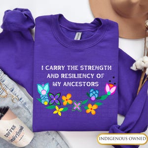 May include: Purple sweatshirt with the text "I carry the strength and resiliency of my ancestors" and a floral design. The sweatshirt is indigenous owned.
