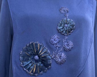 May include: A blue long-sleeved dress with a velvet neckline and embroidered floral details. The flowers are made of blue fabric and have a gold center.