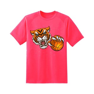 May include: A bright pink t-shirt with a cartoon tiger wearing a basketball jersey and holding a basketball. The tiger has an orange and black striped pattern and a fierce expression.