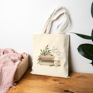May include: A cream-coloured canvas tote bag featuring a printed illustration of a stack of three books topped with olive branches and a coffee mug. The text reads A quieter brighter me, with Good things take time on the bottom book spine.