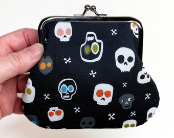 May include: A black coin purse with a silver clasp. The purse is decorated with a repeating pattern of white skulls with colorful details.