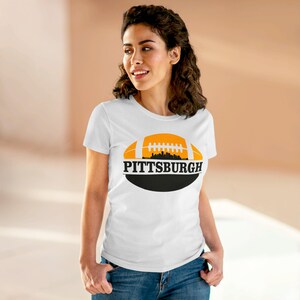 May include: White t-shirt with a black and orange graphic of a football with the city skyline and the text "PITTSBURGH" on it.