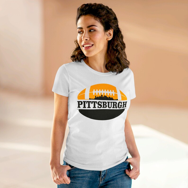 May include: White t-shirt with a black and orange graphic of a football with the city skyline and the text "PITTSBURGH" on it.