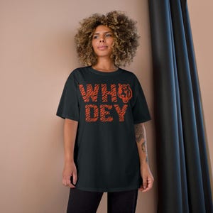 May include: Black t-shirt with an orange tiger stripe design that says "WHO DEY" with a tiger head graphic.
