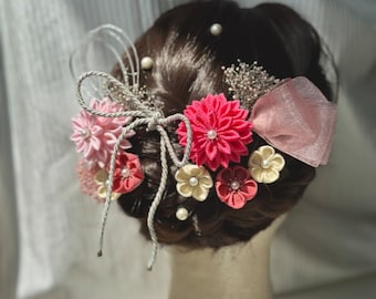 Puede incluir: Un adorno tradicional para el cabello japonés con flores de tela rosa y blanca, una cinta rosa y detalles de cuerda plateada.