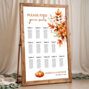 May include: A wooden framed seating chart with the text "PLEASE FIND your seats". The chart features a watercolor design of pumpkins and autumn leaves. The names are listed under table numbers 1-12. The names Isabella & Nathan and the date November 16, 2026 are also displayed.