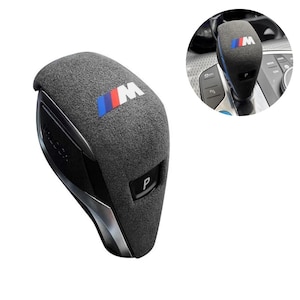 Puede incluir: Un pomo de palanca de cambios de coche gris con el logotipo BMW M en azul, rojo y blanco. El pomo tiene una superficie texturizada y un botón 'P' negro. El diseño incluye un acento plateado y una base negra.