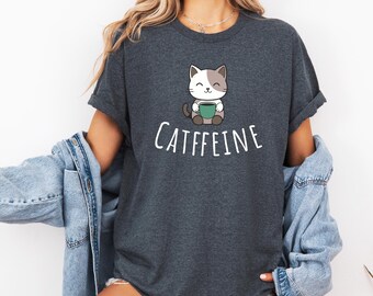 May include: A dark heather gray t-shirt with a cartoon cat holding a cup of coffee. The text "CATFFEINE" is printed below the cat.