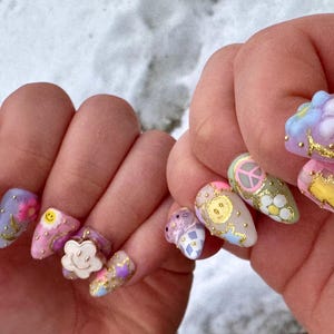 May include: Close-up of a hand with colourful, decorated fingernails. The nails are painted in various pastel colours and feature designs such as flowers, smiley faces, stars, and peace signs.