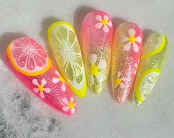 May include: Five long, glittery acrylic nails with a summer theme. Designs include pink and yellow citrus fruit slices, and white daisy flowers with yellow centres. The nails have a glossy finish.