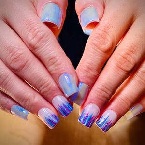 May include: Close-up of a hand with blue and white nail polish. The nails are decorated with a blue and white marble design and a blue and purple glitter design.