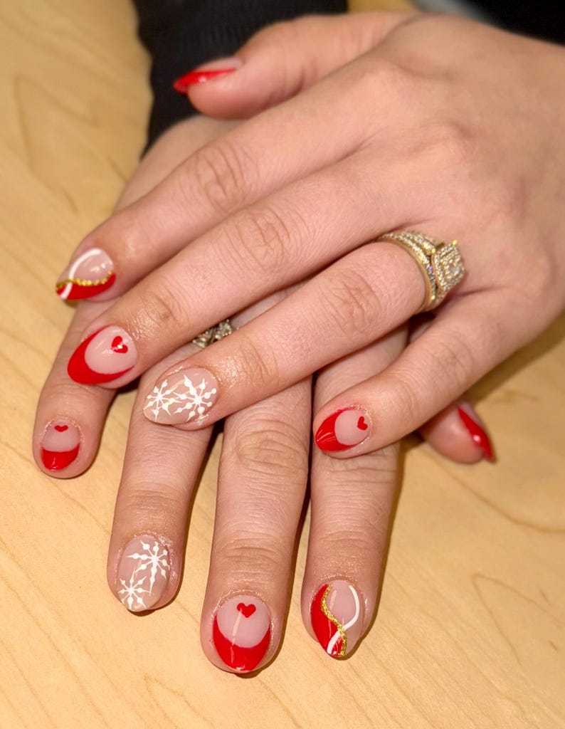 May include: Close-up of hands with red and white nail polish. The nails are decorated with hearts, snowflakes, and gold accents.