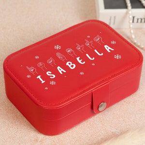 May include: Red jewelry box with a white design of the name "ISABELLA" spelled out in American Sign Language. The box has a snowflake pattern and a silver clasp.