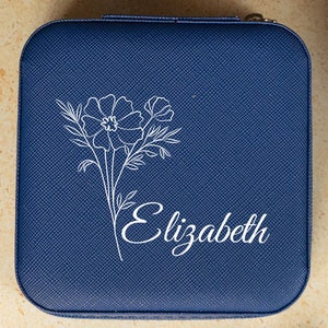 May include: A blue velvet jewelry box with a white floral design and the name "Elizabeth" inscribed on the front.