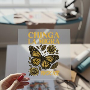 May include: A clear, square sticker featuring a detailed illustration of a butterfly with sunflowers and leaves. The text "CHINGA LA MIGRA" and "FUCK ICE" are in yellow. The butterfly has yellow and black details.