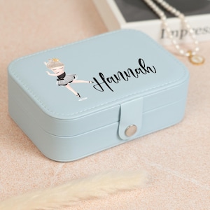 May include: A light blue jewelry box with a ballerina graphic and the name "Hannah" in black script. The box has a rectangular shape with a clasp closure. The ballerina is wearing a black leotard and a silver tutu.