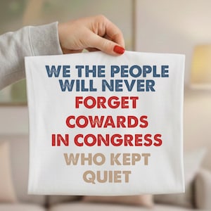 May include: A white square textile with the text "WE THE PEOPLE WILL NEVER FORGET COWARDS IN CONGRESS WHO KEPT QUIET" in blue, red, and tan lettering. The textile is held up by a person.