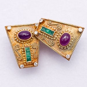 May include: A pair of gold earrings with green and purple gemstones. The earrings are intricately designed with a geometric pattern and have a vintage look.
