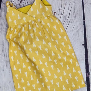 May include: A yellow sundress with white lobster print. The dress features a V-neckline, braided straps, and a gathered waist. The fabric has a soft texture, and the overall design is casual and summery.