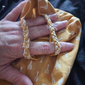 May include: A yellow fabric bag with a white lobster pattern. The bag has braided handles in yellow and white. The bag is held open, revealing the inside.