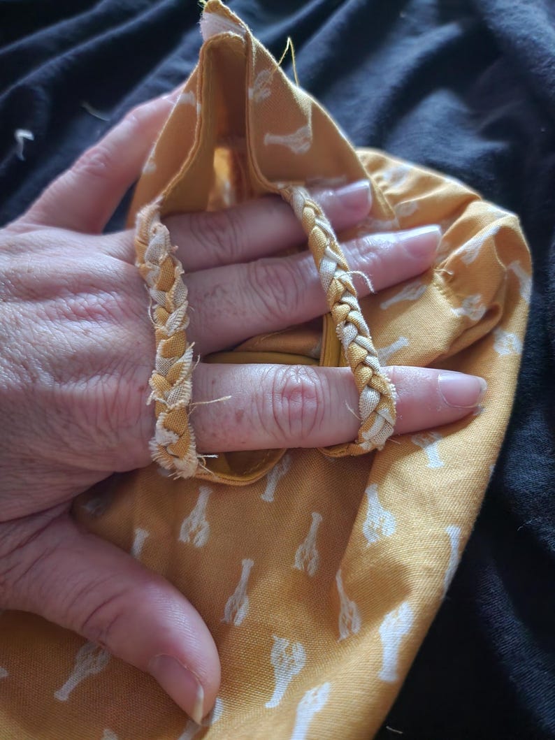 May include: A yellow fabric bag with a white lobster pattern. The bag has braided handles in yellow and white. The bag is held open, revealing the inside.
