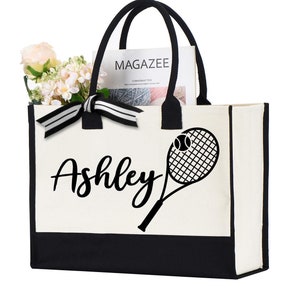 May include: A white canvas tote bag with black trim and handles. The bag has a black tennis racket and ball design with the name "Ashley" printed on the front.