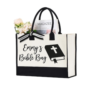 May include: A white canvas tote bag with black trim and handles. The bag has a black and white image of a book with a cross on the cover and the text "Emmy's Bible Bag".