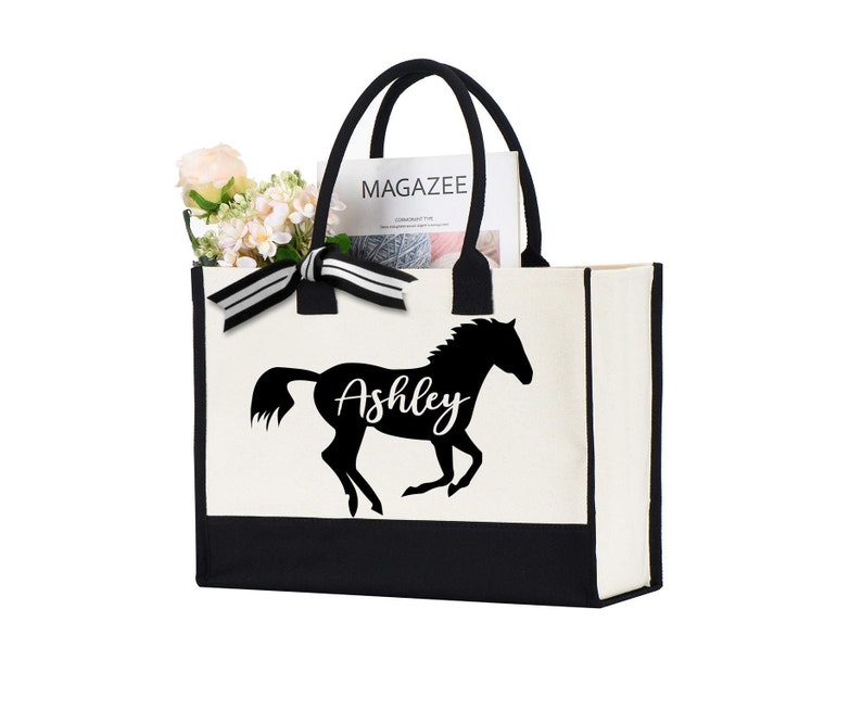 May include: A white canvas tote bag with black trim and handles. The bag has a black silhouette of a horse with the name "Ashley" printed on it.