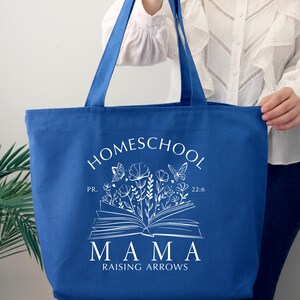 Puede incluir: Una bolsa de tela azul real con texto blanco que dice "Homeschool Mama Raising Arrows" con un dise&ntilde;o floral y un libro abierto con mariposas. El texto "PR. 22:6" tambi&eacute;n est&aacute; incluido.