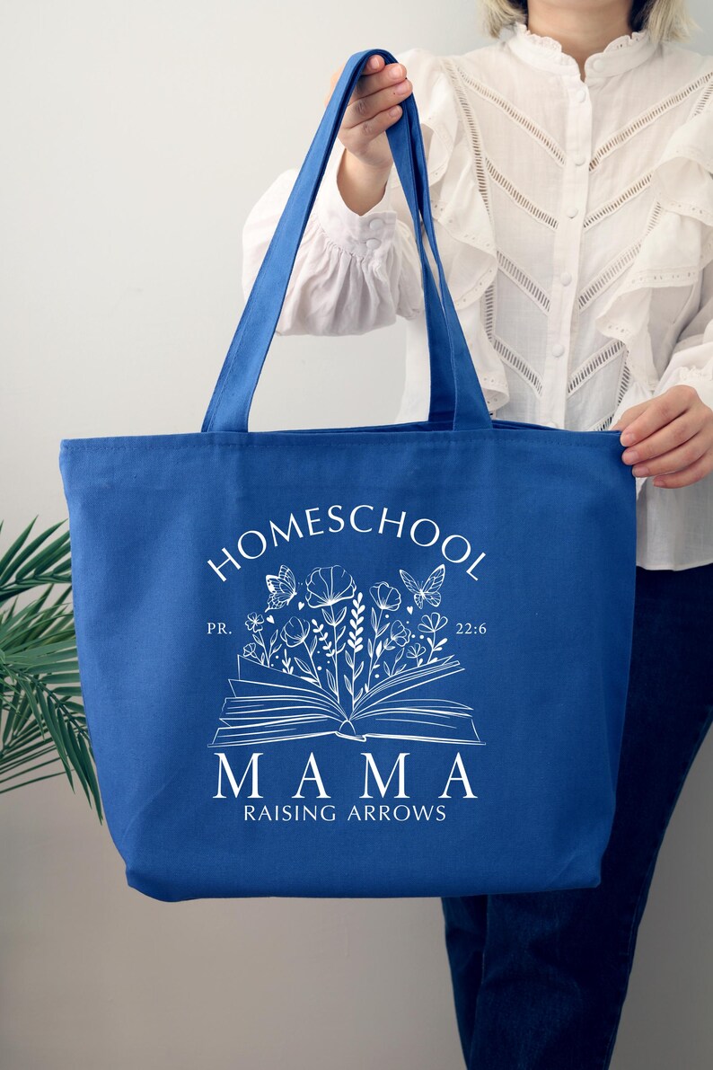 Puede incluir: Una bolsa de tela azul real con texto blanco que dice "Homeschool Mama Raising Arrows" con un dise&ntilde;o floral y un libro abierto con mariposas. El texto "PR. 22:6" tambi&eacute;n est&aacute; incluido.