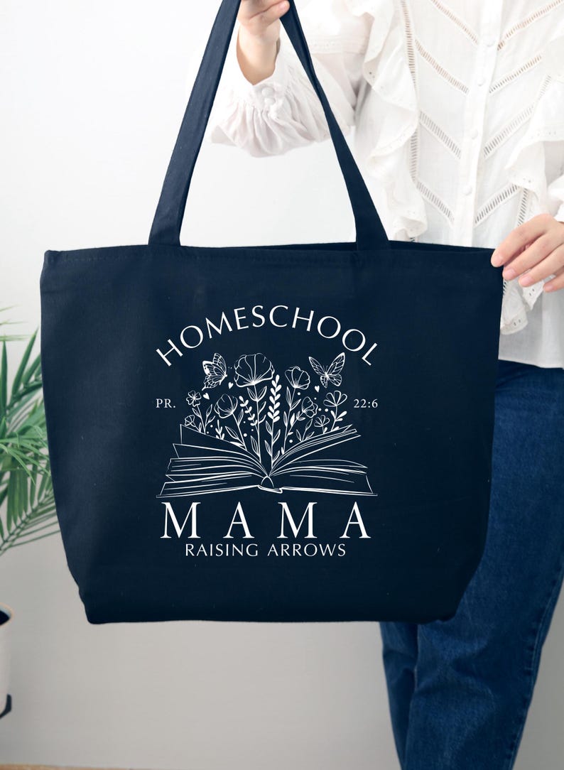 Puede incluir: Bolsa de lona negra con texto blanco que dice "Homeschool Mama Raising Arrows" con un dise&ntilde;o floral y un libro abierto con mariposas.