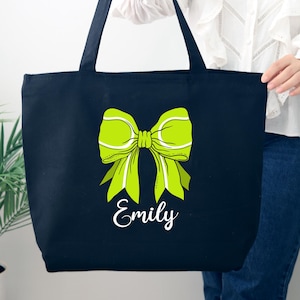 May include: Black canvas tote bag with a green tennis ball bow and the name "Emily" printed in white.