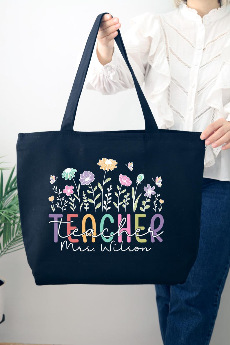 May include: Black canvas tote bag with a colorful floral design and the text "teacher mrs. wilson".
