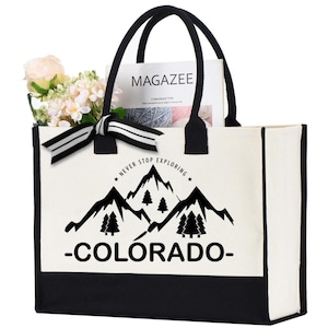 May include: A white canvas tote bag with black trim and handles. The bag has a black and white graphic of mountains and trees with the text "Never Stop Exploring - Colorado -" printed on the front.
