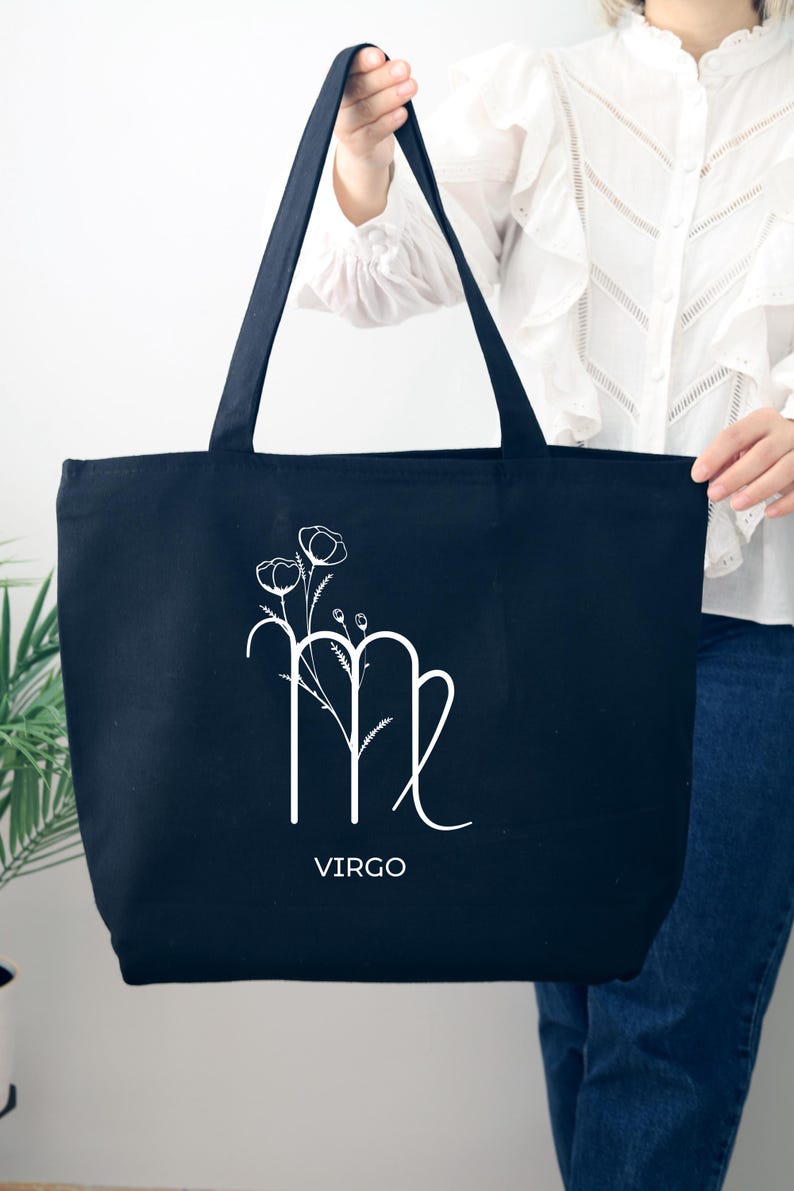 May include: Black canvas tote bag with a white floral design and the Virgo zodiac symbol. The text "VIRGO" is printed below the symbol.