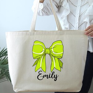 May include: A large, natural-colored canvas tote bag with a green bow and the name "Emily" printed in black.