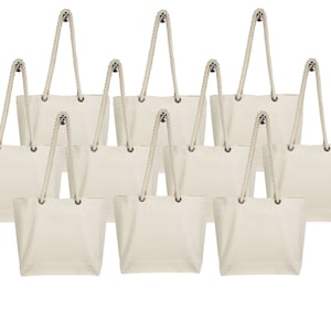 May include: Set of ten blank canvas tote bags with rope handles. The bags are a natural off-white color.