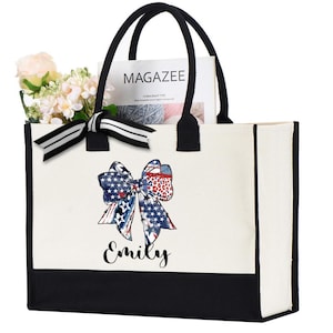 May include: A white canvas tote bag with black handles and a black bottom. The bag features a patriotic bow design with the name "Emily" printed below. The bag is filled with flowers and a magazine.