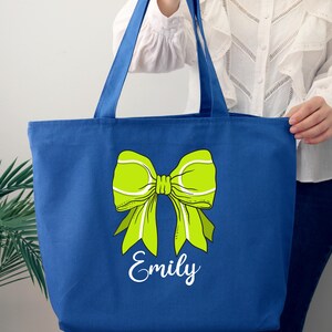 May include: A royal blue tote bag with a green tennis ball bow and the name "Emily" printed in white.